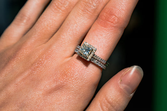 A close-up of a hand wearing a sparkling bespoke square-cut diamond engagement ring with a pavé diamond band, paired with a matching pavé wedding band.