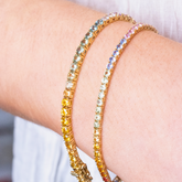 A wrist adorned with two stunning, multi-coloured lab-grown sapphire tennis bracelets set in yellow gold, highlighting the sustainable luxury jewellery collection at Griffin & Co.