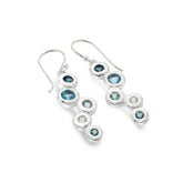 A close-up, high-angle shot of a pair of sterling silver drop earrings featuring multiple round blue and white topaz stones set in an organic, cascading design. The earrings are displayed on a white background.