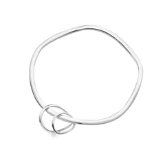 A studio shot of a polished silver bangle with a wavy, irregular shape and two interlinked circles at the bottom. The bangle is casting a shadow on a white background.