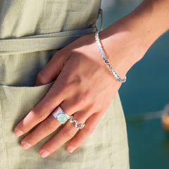 A close-up of a person's hand wearing the multi-heart bangle and a large ring with a light-colored stone, with a pocket in the foreground.