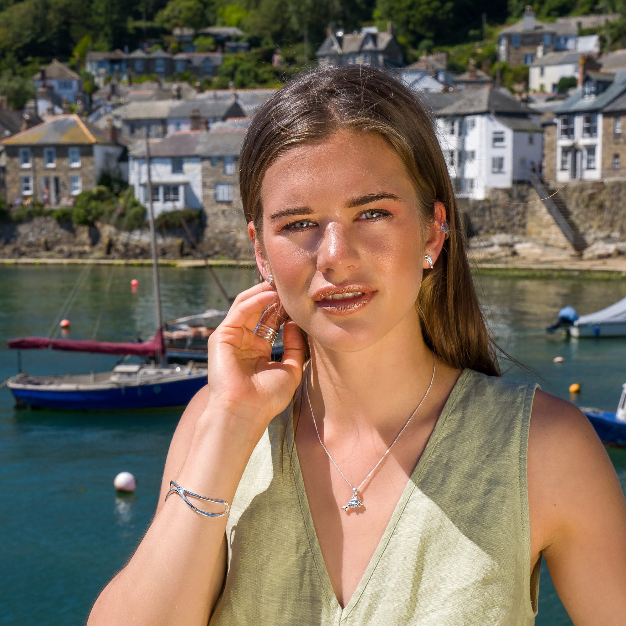 A woman standing in front of a harbour wearing silver dolphin stud earrings and a matching pendant necklace.
