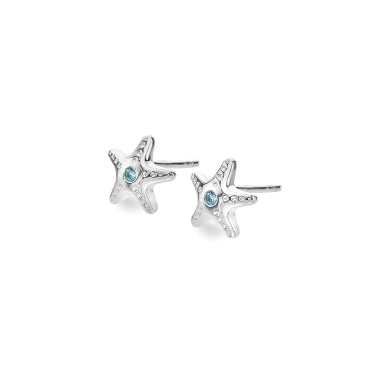 A pair of petite sterling silver starfish stud earrings, each set with a central round blue topaz gemstone, on a white background. 1800