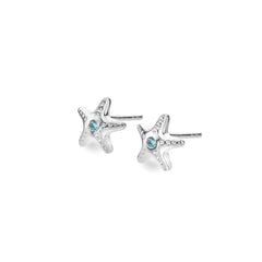 A pair of petite sterling silver starfish stud earrings, each set with a central round blue topaz gemstone, on a white background.