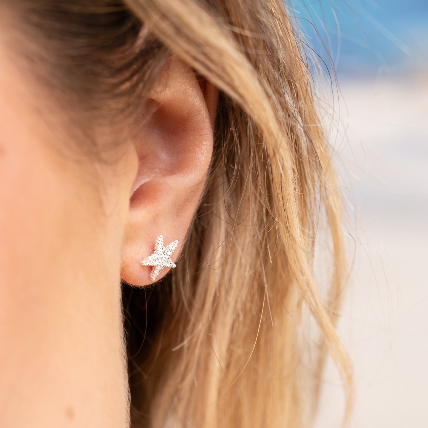 A close-up of a woman's ear wearing a silver starfish stud earring.