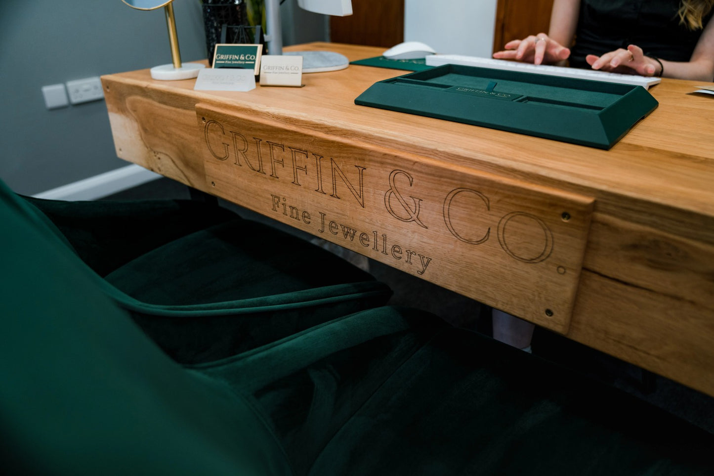 Wooden counter with 'Griffin & Co Fine Jewellery' branding, green chair, and person partially visible.