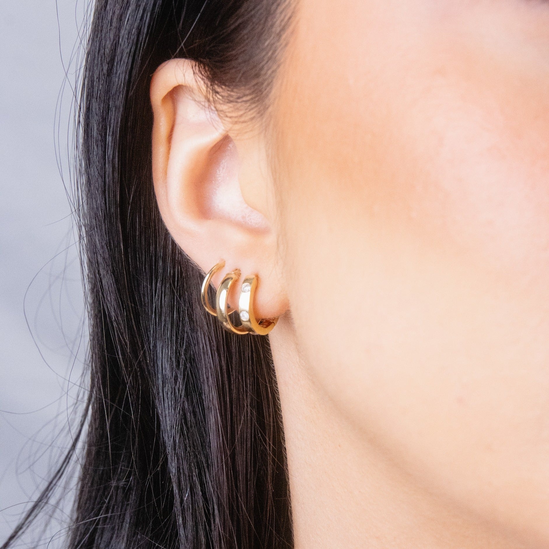 Close-up of a person wearing gold hoop earrings with a neutral background