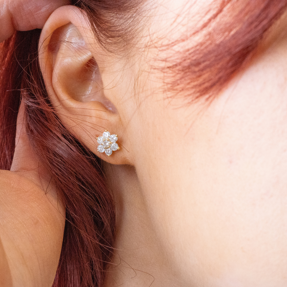 A close-up of a model wearing lab-grown diamond flower cluster stud earrings in yellow gold from Griffin & Co, showcasing an ethical and brilliant fine jewellery option available in Chichester.