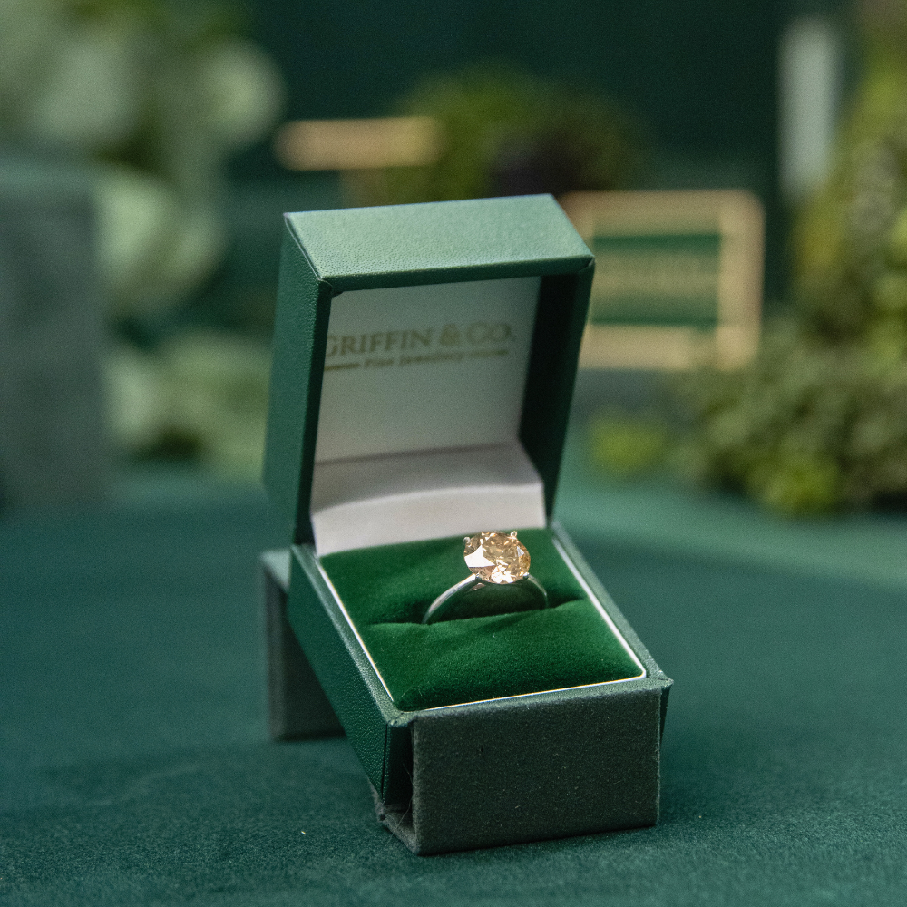 A stunning bespoke lab-grown diamond engagement ring with a beautiful cushion-cut stone, presented in the signature green Griffin & Co jewellery box, representing custom-designed ethical luxury from our Chichester store.
