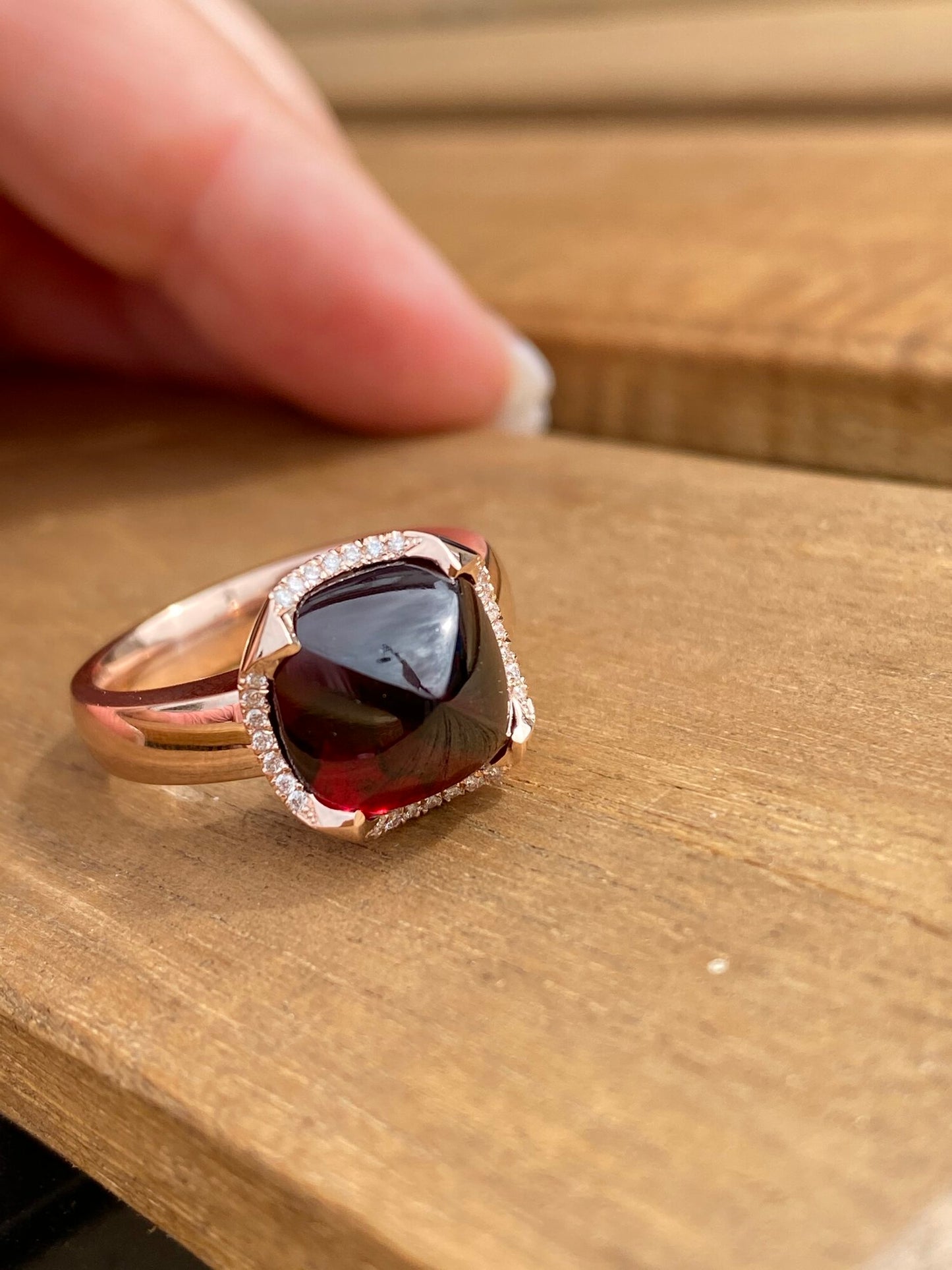 Rose gold ring with a large gemstone held over a wooden surface