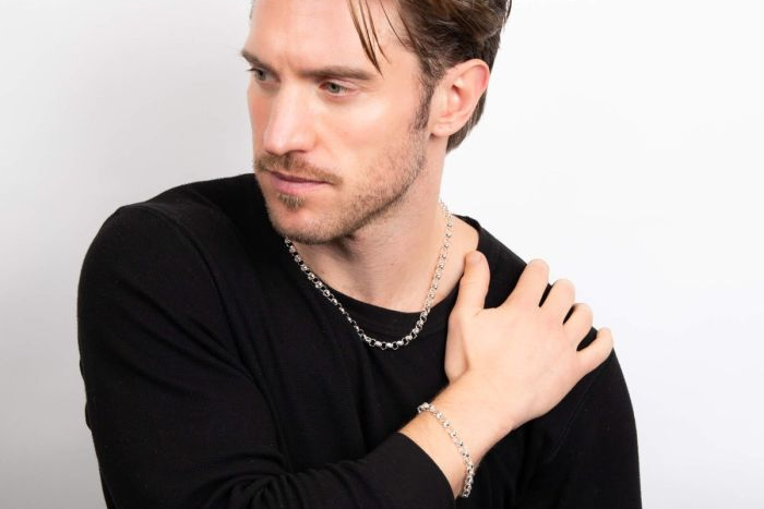 Man wearing a black shirt with a silver chain and bracelet on a white background