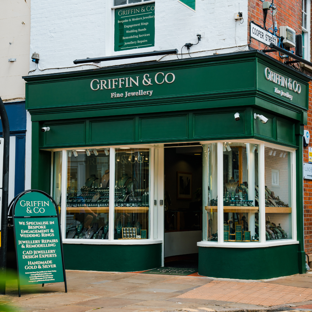 A street-level view of the Griffin & Co Fine Jewellery shop front. The elegant dark green facade features large display windows and its name in silver lettering. An A-frame sign on the pavement lists their specialities.