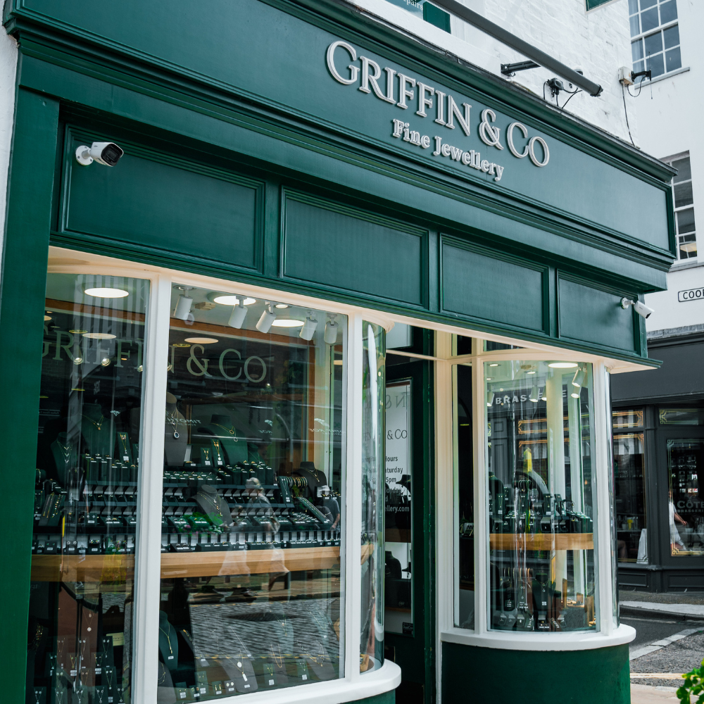 An angled close-up of the Griffin & Co storefront, focusing on the main sign with silver lettering and the brightly lit, curved display windows filled with a wide selection of jewellery.