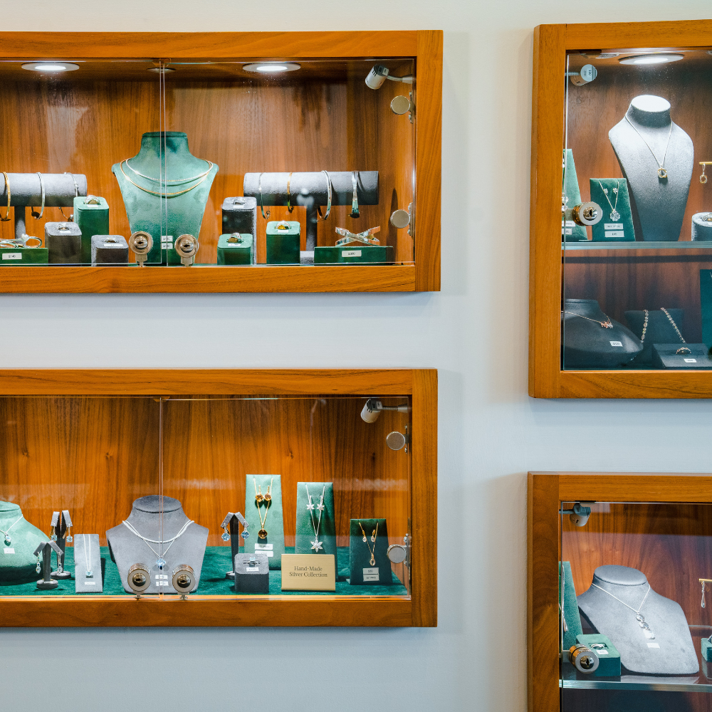 Four wood-framed, wall-mounted display cabinets showcasing various jewellery collections. Each case is internally lit and contains necklaces and other items on display stands against a dark background.