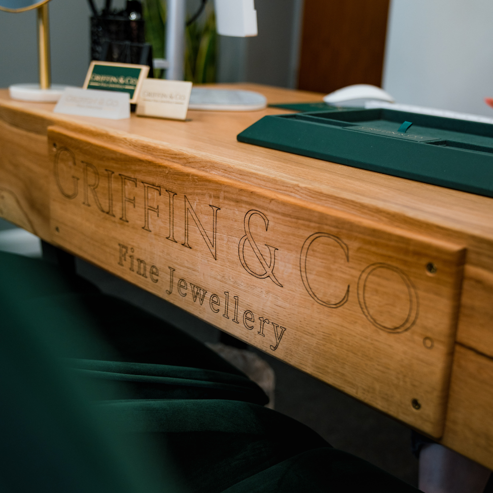 A close-up of a wooden workbench, showing the 'GRIFFIN & CO Fine Jewellery' name and logo engraved into the side panel.