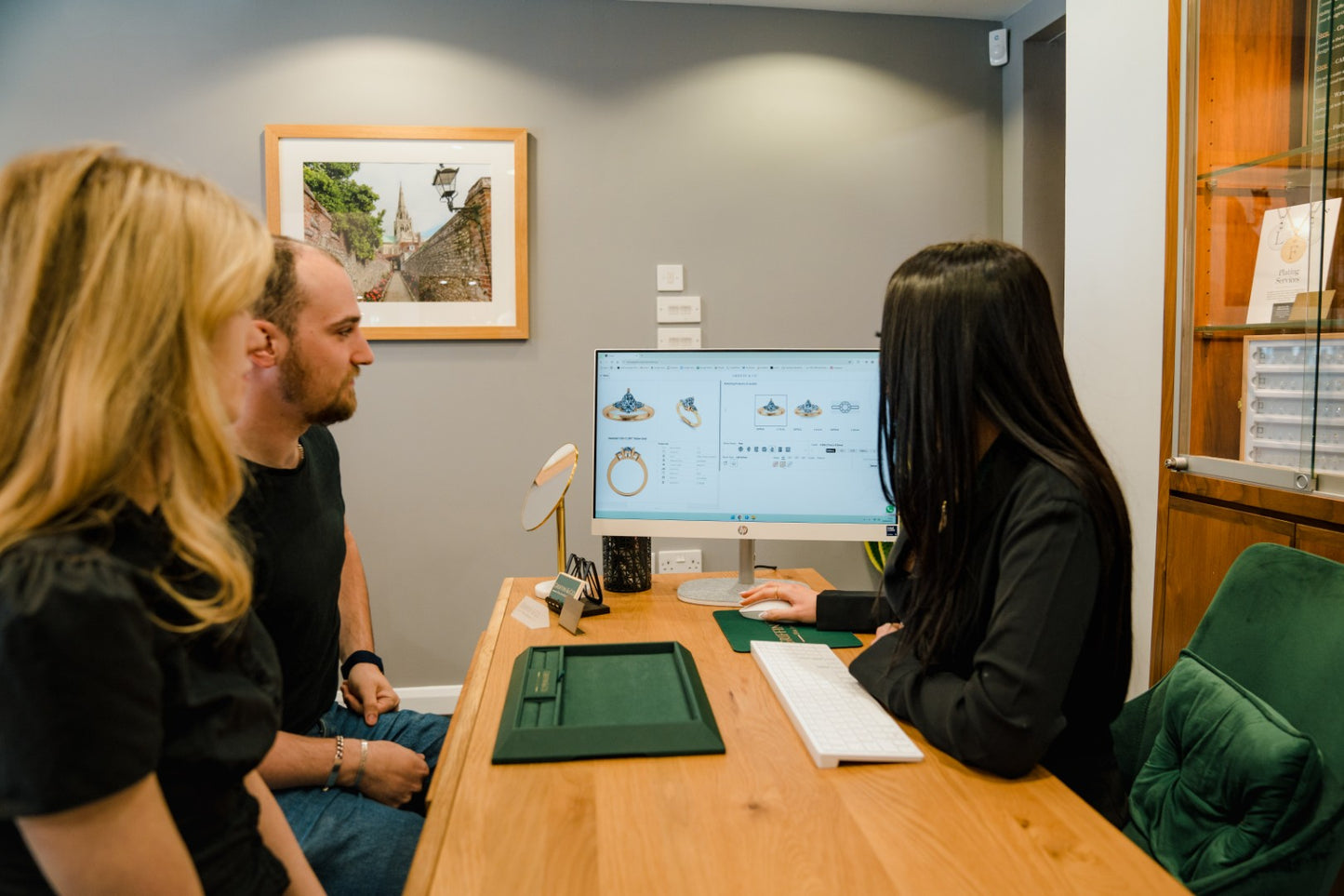 3 people sitting at a desk with a computer, engaged in a discussion regarding design a bespoke ring design.