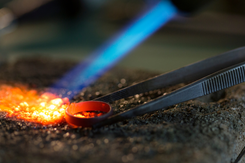 Close-up of aForge with glowing metal and a torch, jeweller repairs.