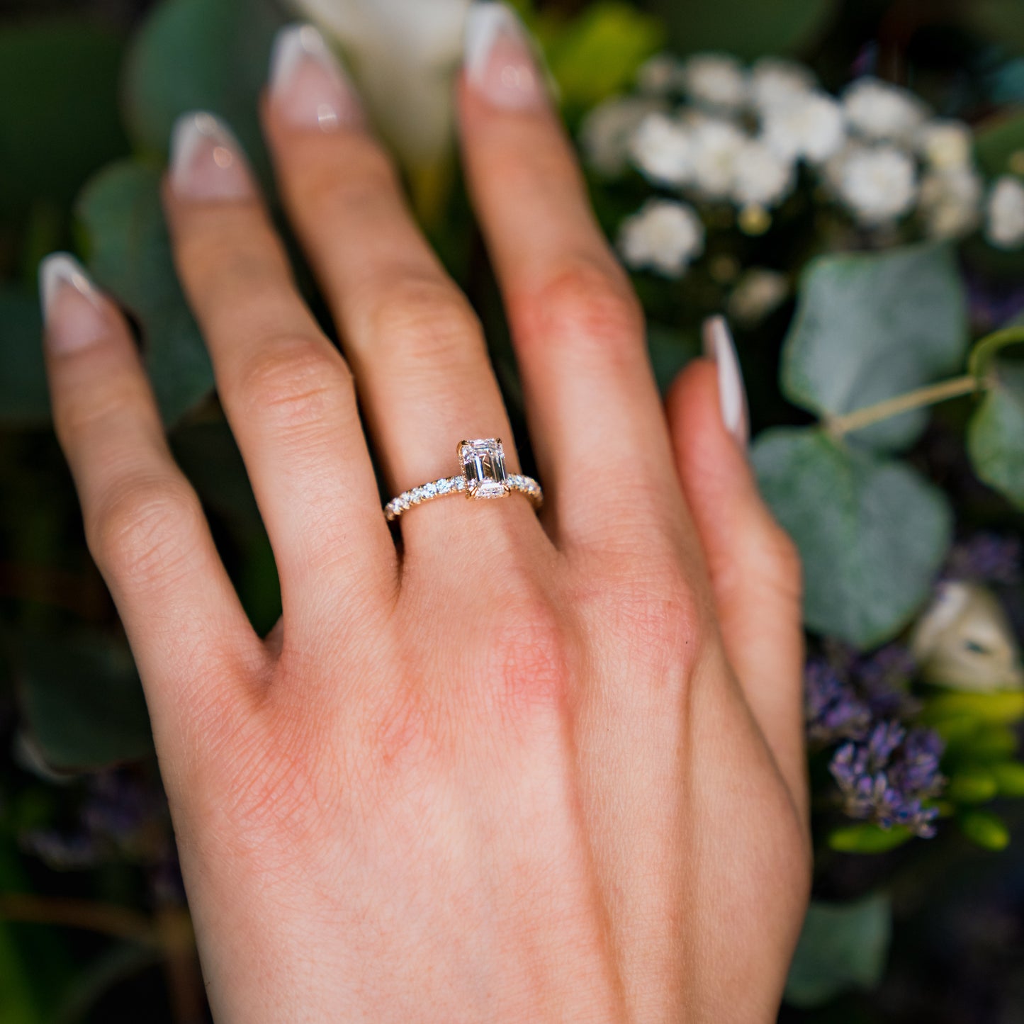 Hand wearing a diamond ring with a blurred floral background