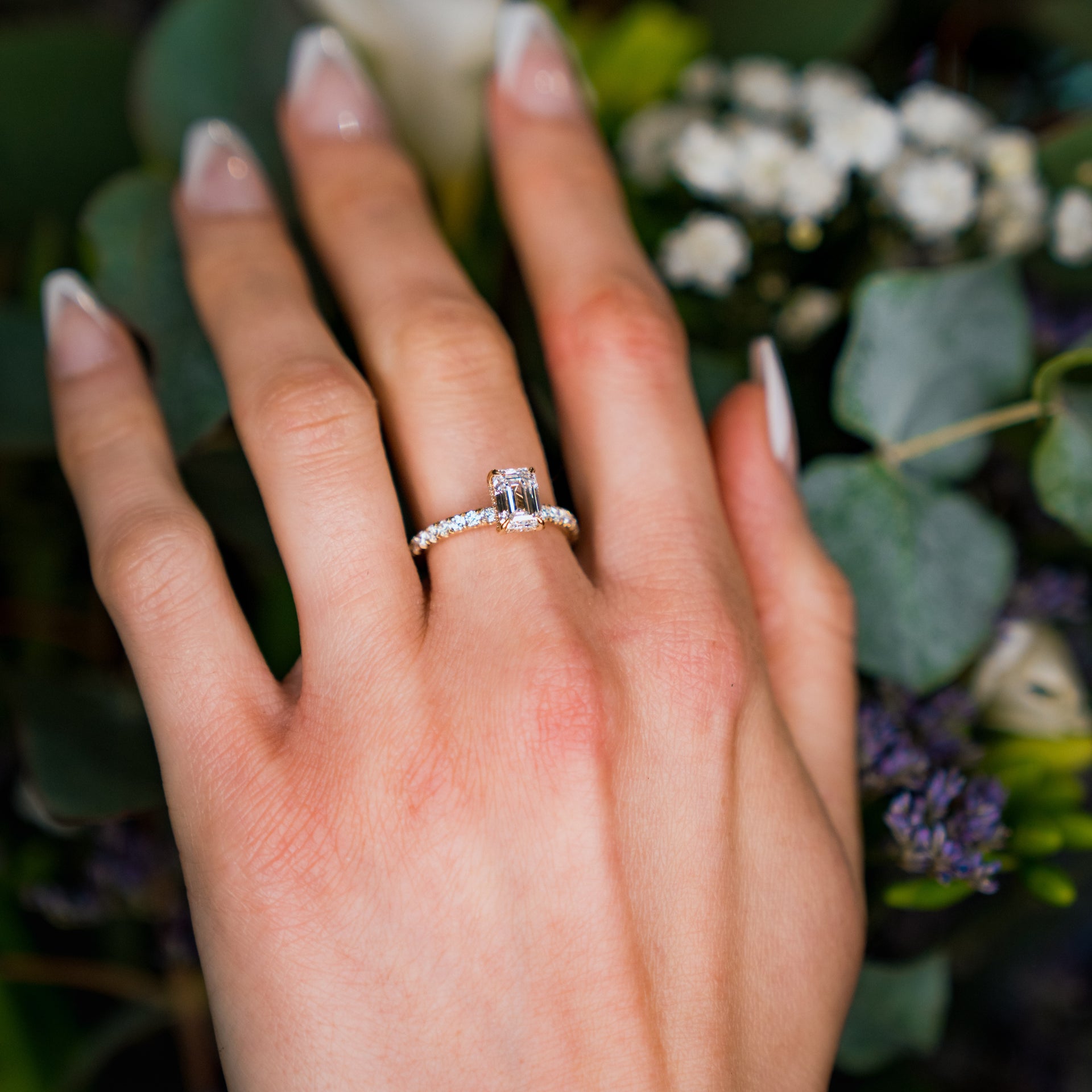 Hand wearing a diamond ring with a blurred floral background