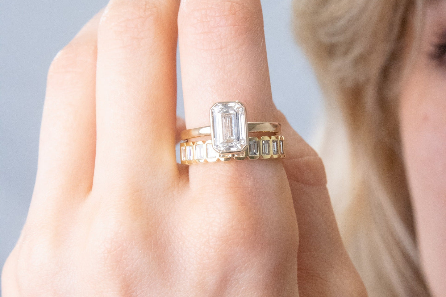 Close-up of a hand wearing a gold ring with a diamond on a light gray background