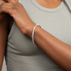 Person wearing a silver bracelet on a neutral background