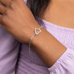 Silver bracelet with a heart design on a wrist, wearing a light purple top.