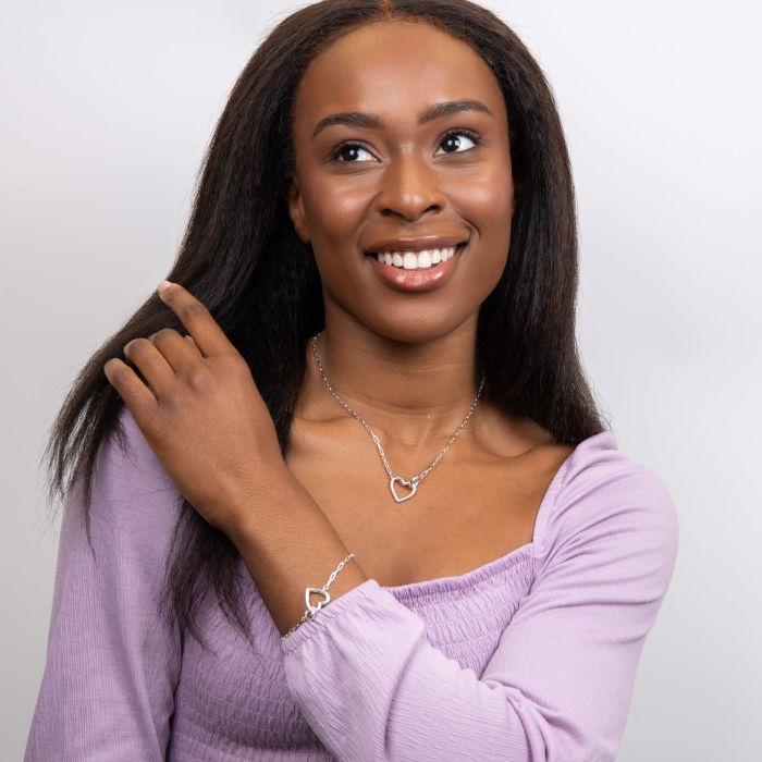 Woman wearing a silver heart necklace and bracelet against a plain background