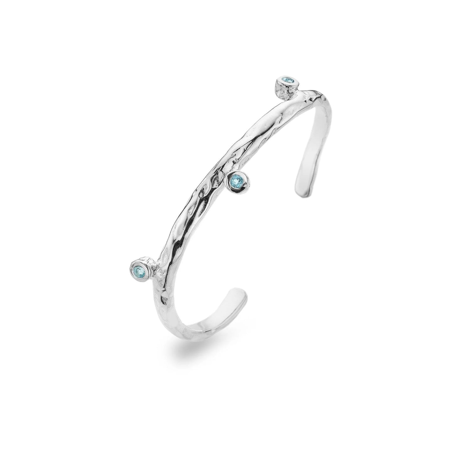 A close-up shot of a chunky sterling silver bangle with a textured surface, similar to a rock, on a white background. Three light blue topaz stones are inlaid into the bangle. The bangle is open at the back.
