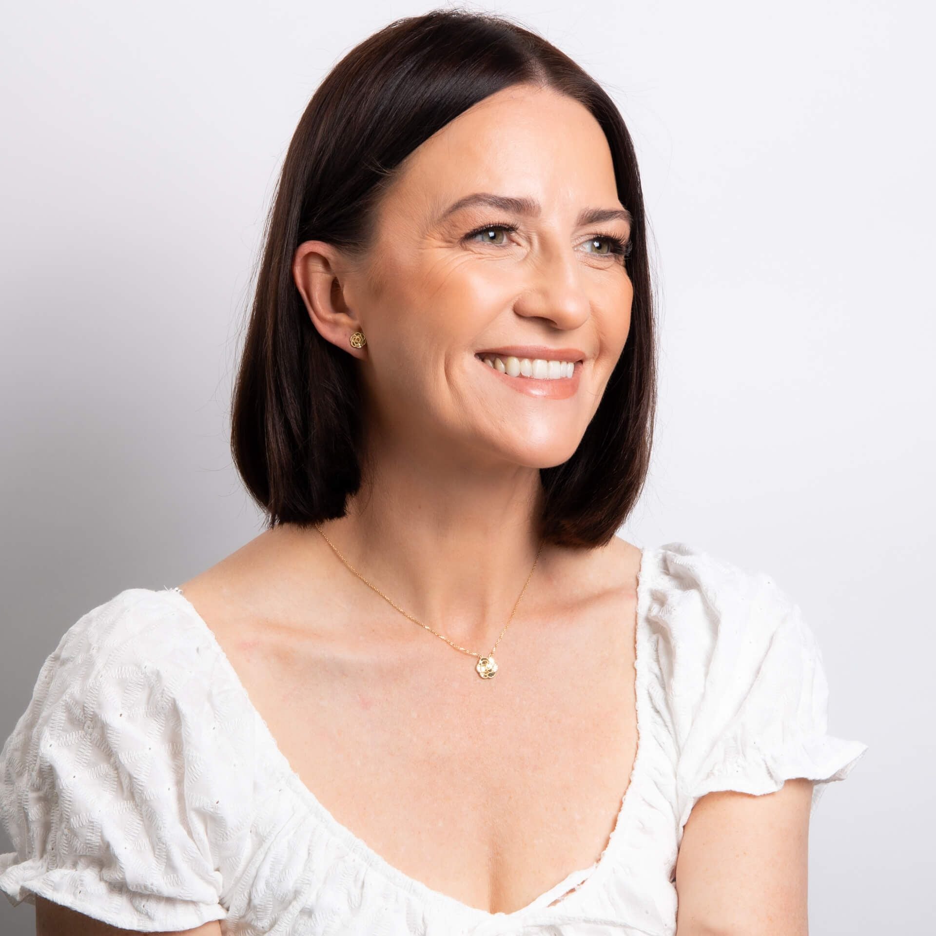 A smiling woman with a bob hairstyle wearing the English Rose necklace and matching stud earrings.