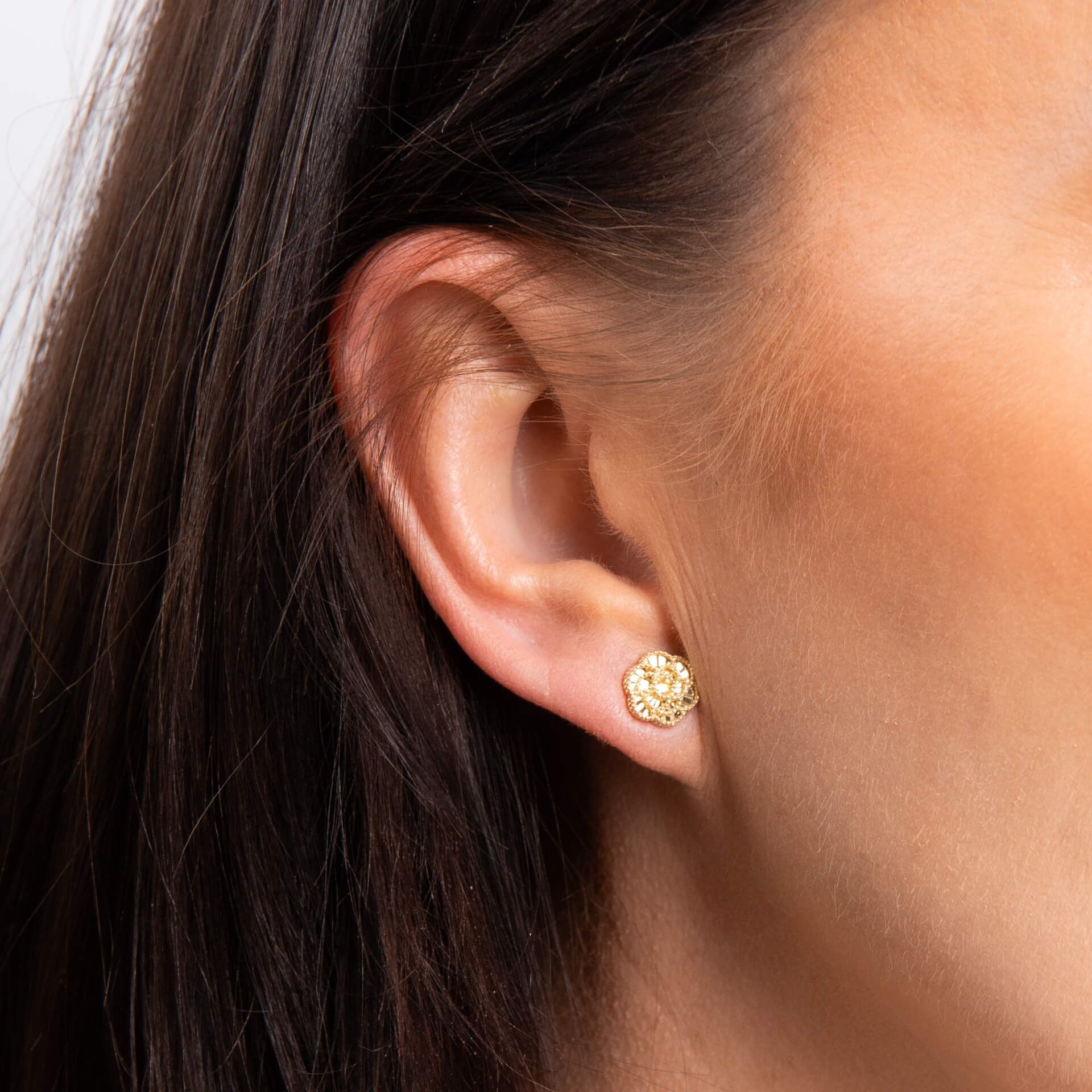 A close-up of a woman's ear wearing a gold English Rose stud earring, with matching necklace visible.