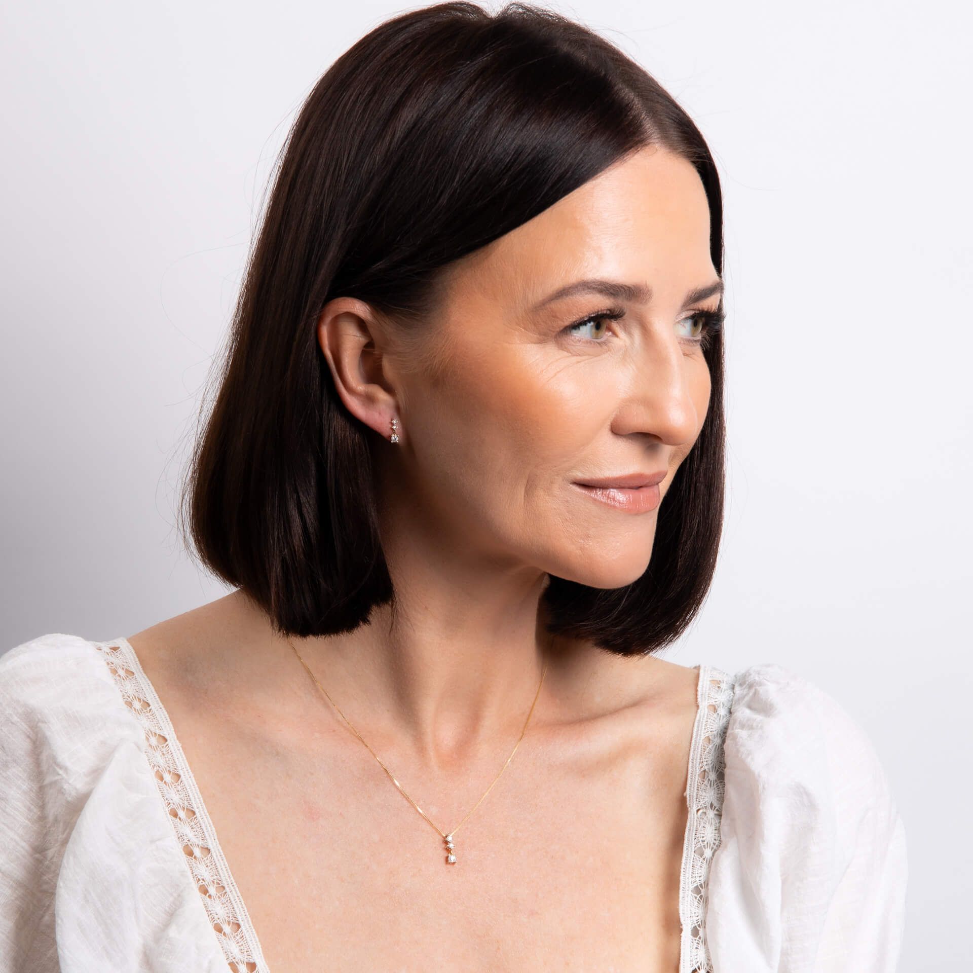 A smiling woman with a bob hairstyle wearing the diamond trilogy pendant and matching drop earrings.