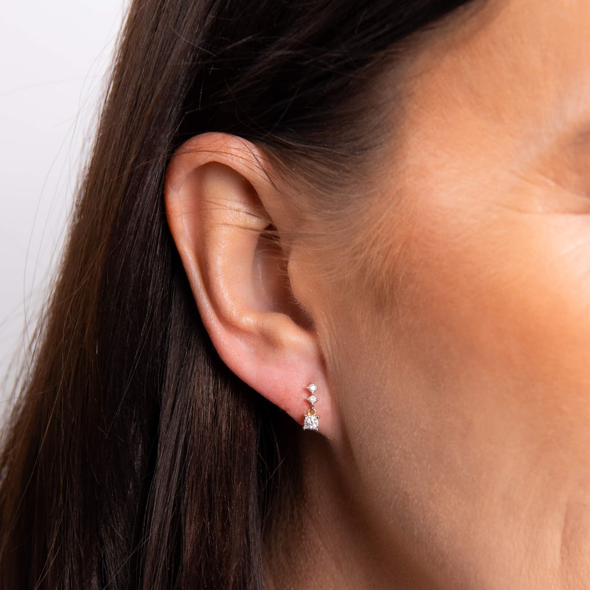 A smiling woman with a bob hairstyle wearing the diamond trilogy drop earrings and matching pendant necklace.