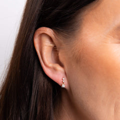 A smiling woman with a bob hairstyle wearing the diamond trilogy drop earrings and matching pendant necklace.