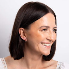A smiling woman with a bob hairstyle wearing the gold double hoop earrings, looking to the side.