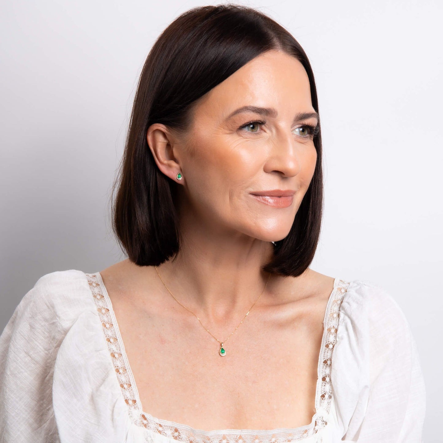 A close-up of a woman's ear wearing an emerald teardrop stud earring with diamond accents.