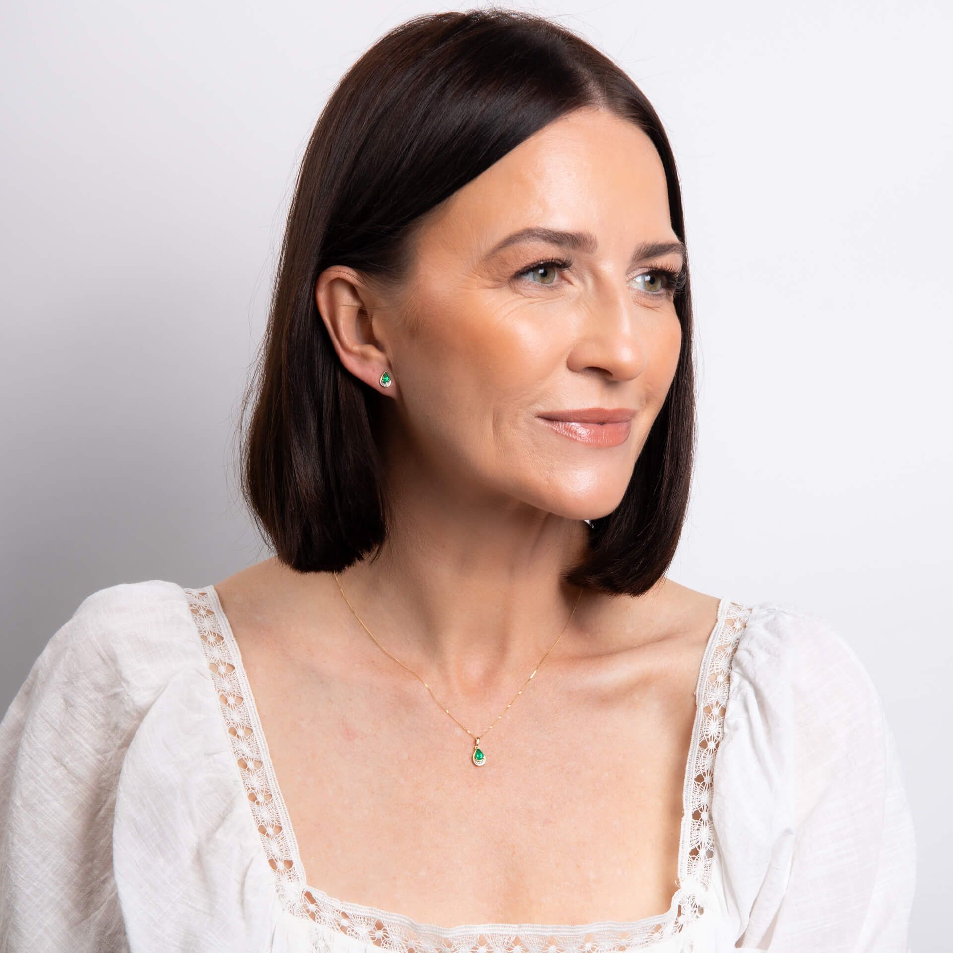 A smiling woman with a bob hairstyle wearing the emerald teardrop pendant and matching stud earrings.
