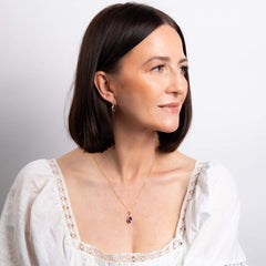 Woman wearing a white blouse with lace details and a necklace on a plain background