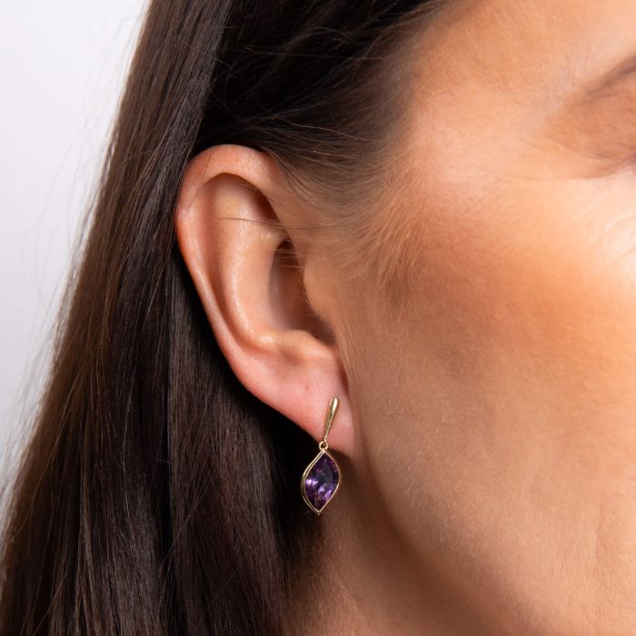 Close-up of an ear wearing a purple teardrop earring with gold setting.