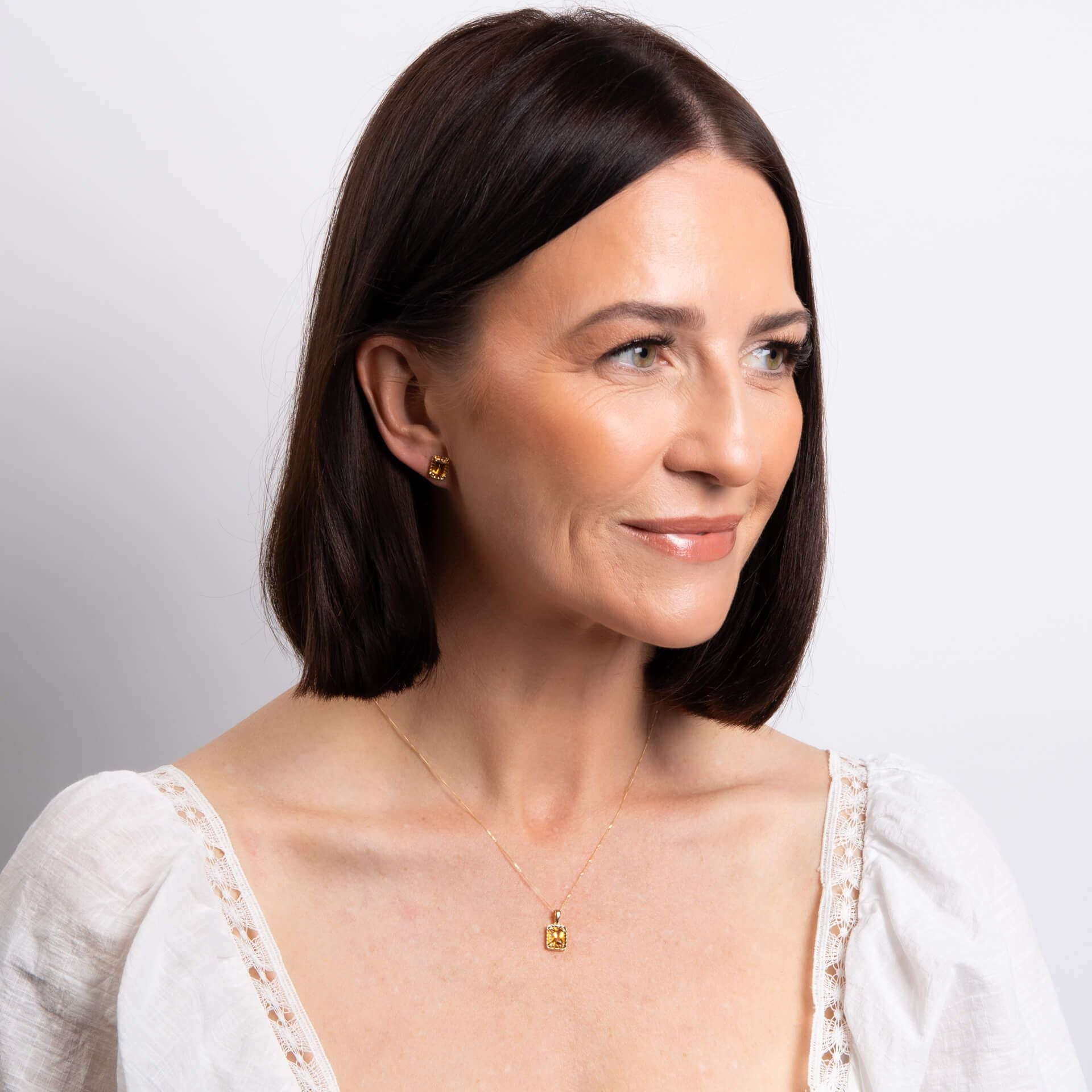 Woman wearing a gold necklace and earrings against a light background