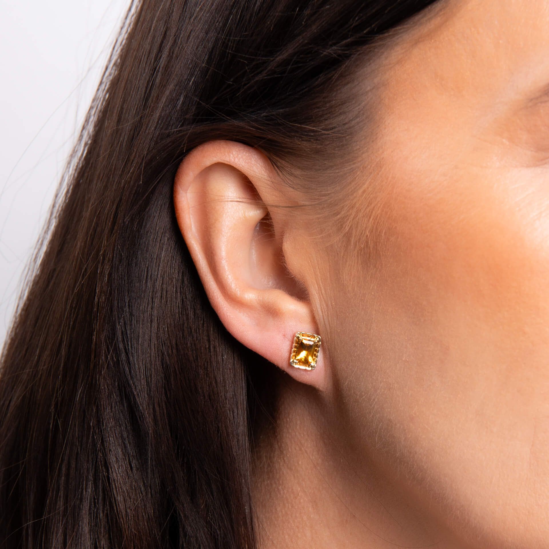 A close-up of a woman's ear wearing a gold citrine octagon stud earring.