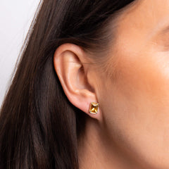 A close-up of a woman's ear wearing a gold citrine octagon stud earring.