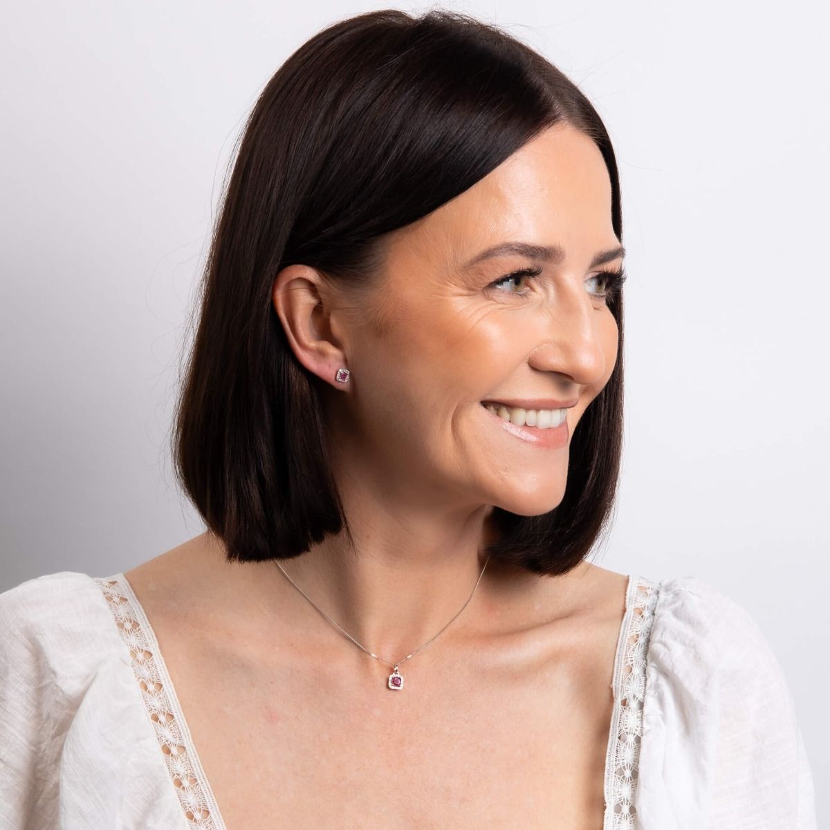 Woman wearing a necklace with a clear pendant on a plain background