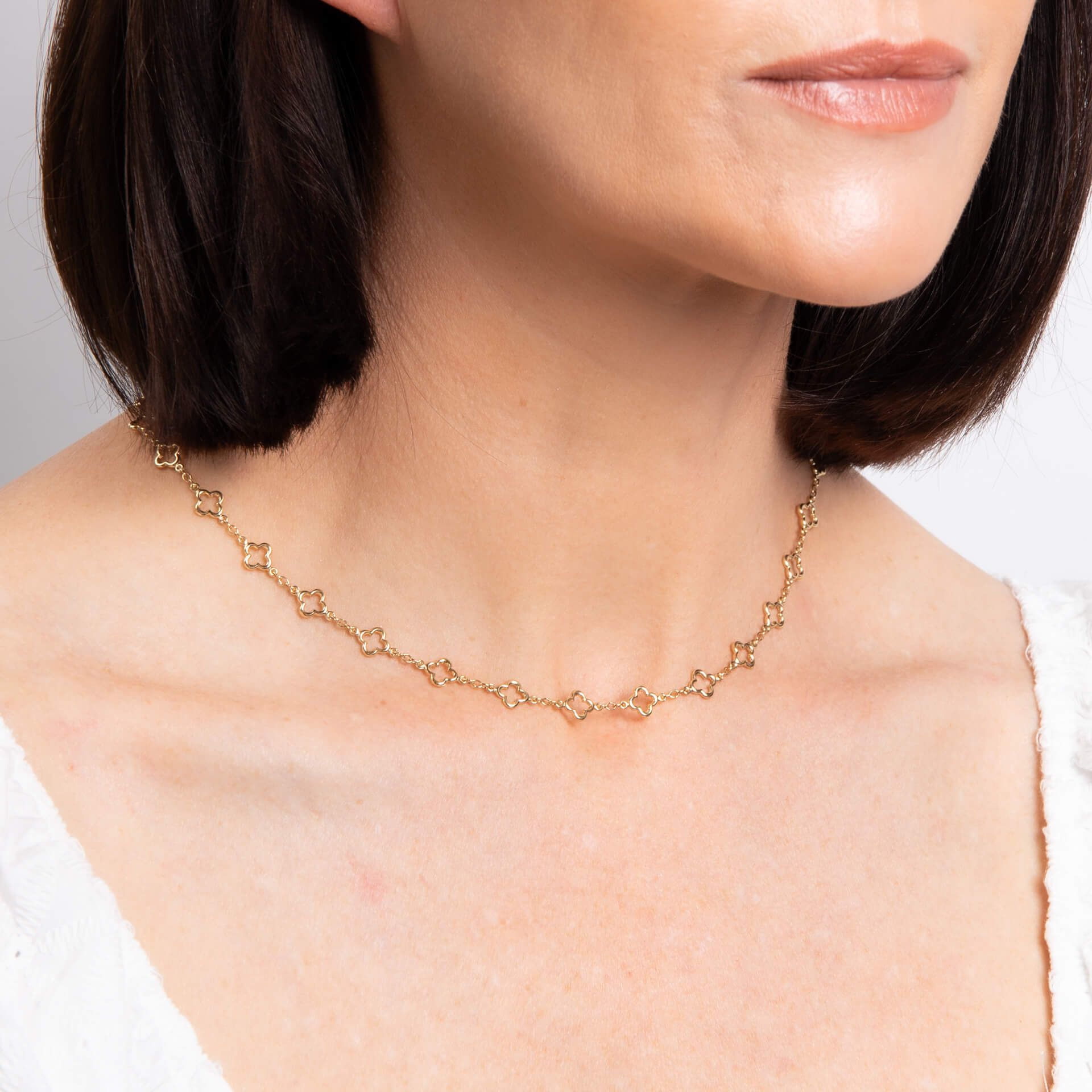 A close-up of a woman's neck wearing the 9ct gold quatrefoil station necklace.