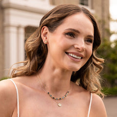 A smiling woman with wavy hair wearing the English Rose pendant necklace layered with a beaded gemstone necklace.