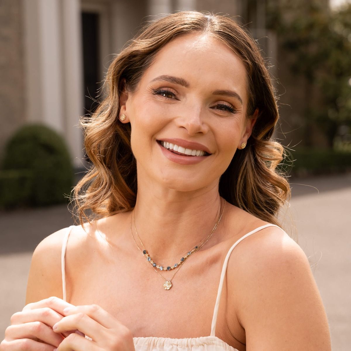A smiling woman wearing the English Rose stud earrings and layered gold necklaces.