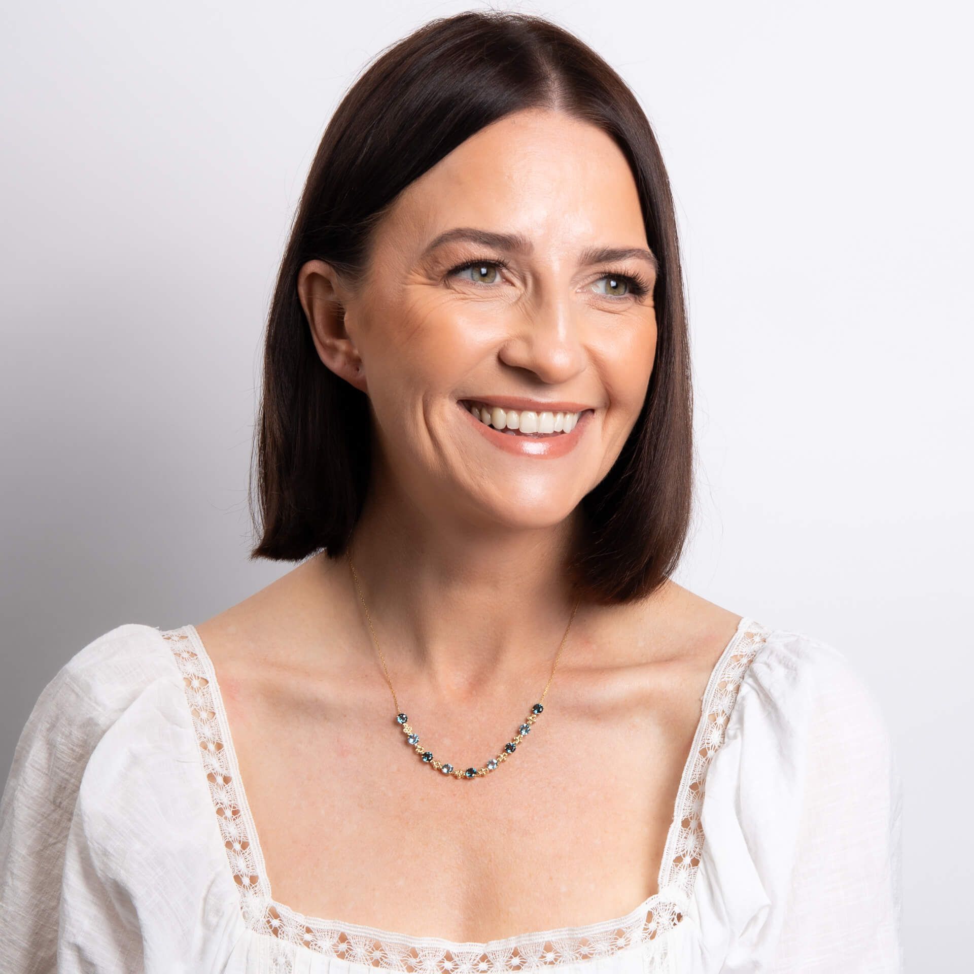 Woman wearing a white blouse with lace details and a necklace on a plain background