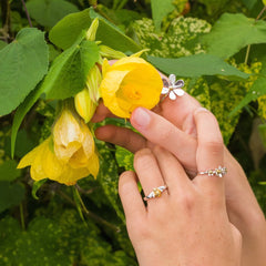 Hand holding a yellow flower with green leaves in the background