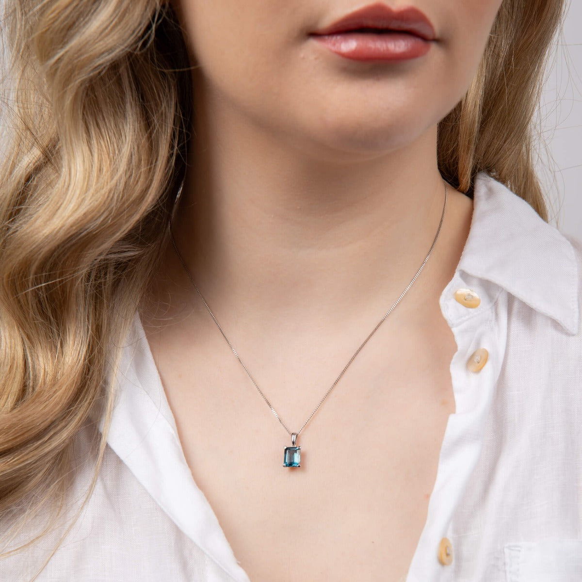 Model wearing rectangle blue topaz pendant in 9ct white gold