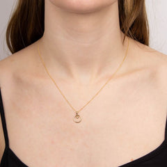 Gold necklace with a small pendant on a person wearing a black top.