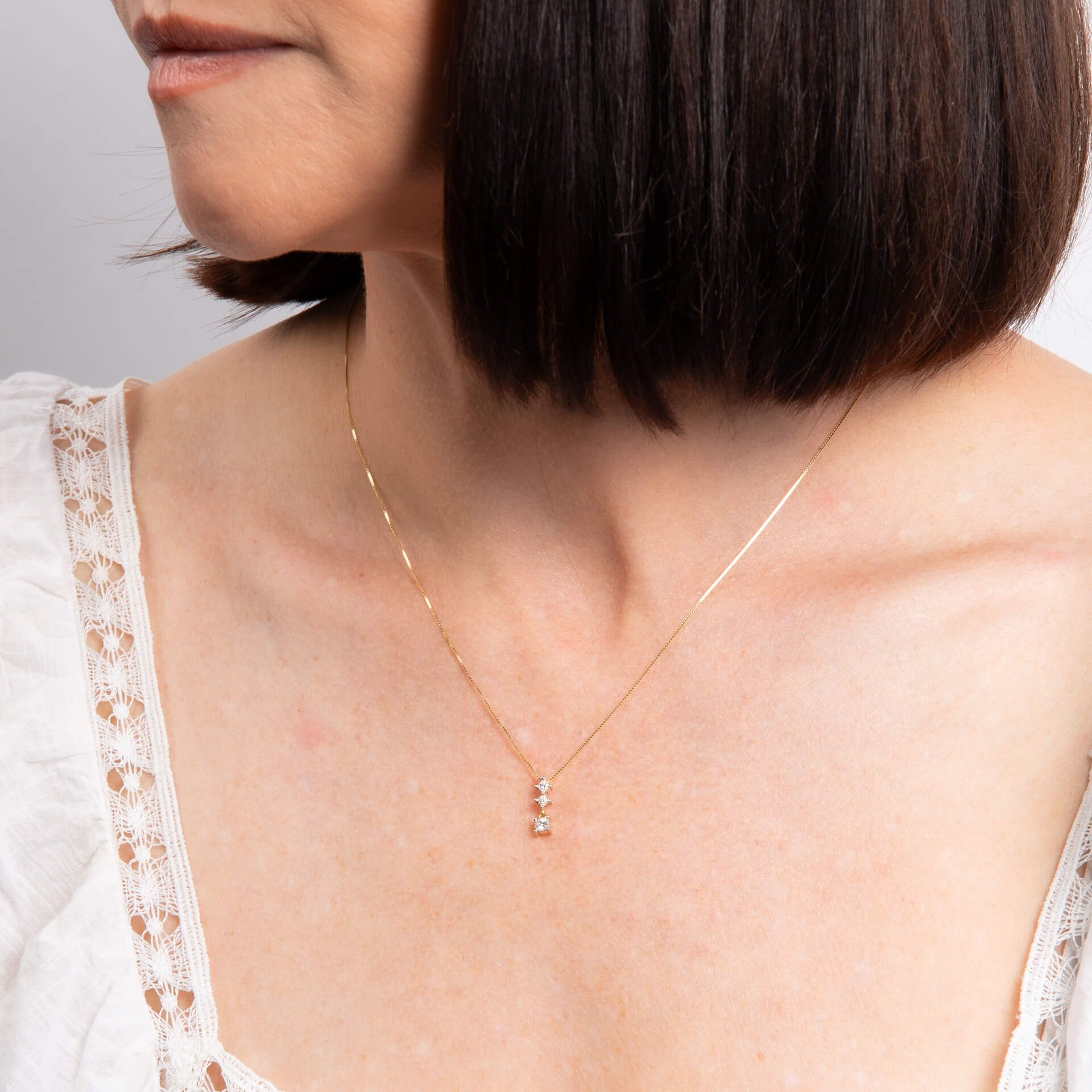 A close-up of a woman's neck wearing the diamond trilogy pendant on a delicate gold chain.